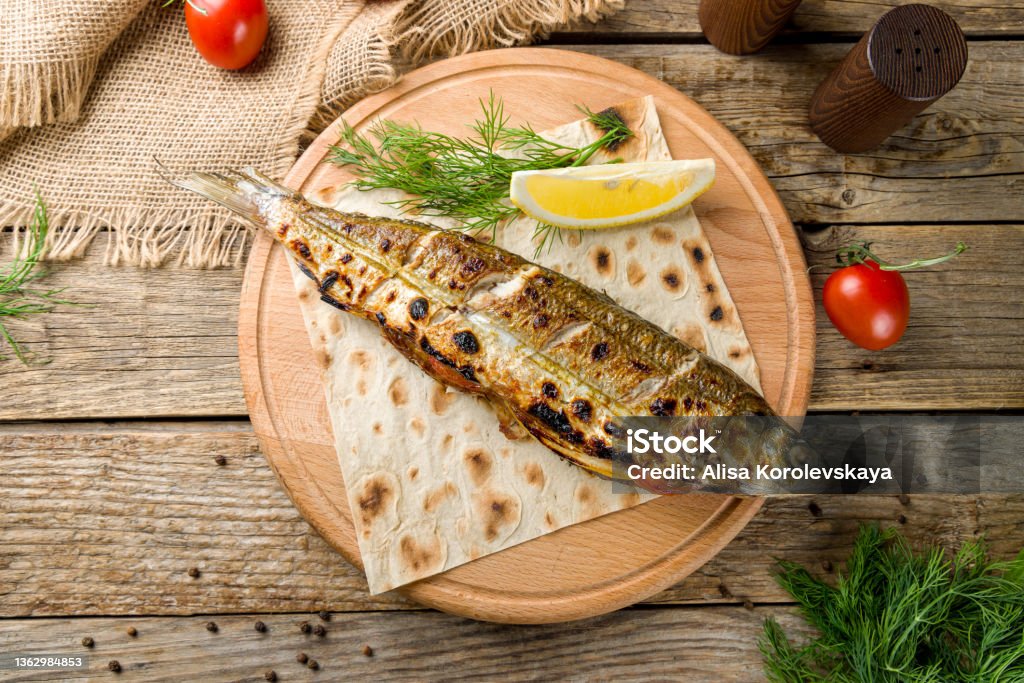 Fried sea bass on the board with lemon top view on old wooden table Sea Bass Stock Photo