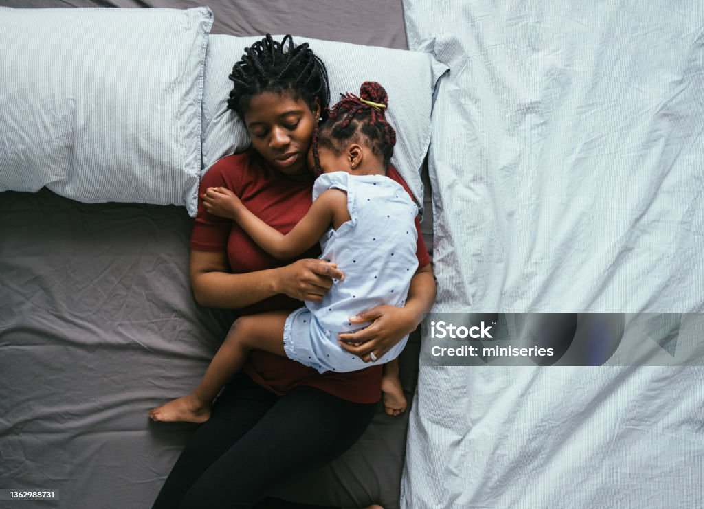 Top View of Beautiful Mother with Little Daughter Sleeping in Bed Directly above photo of tired mother with daughter cuddling and napping together on the bedroom. Mother Stock Photo