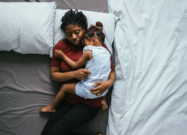 Top View of Beautiful Mother with Little Daughter Sleeping in Bed Directly above photo of tired mother with daughter cuddling and napping together on the bedroom. SLEEP stock pictures, royalty-free photos & images