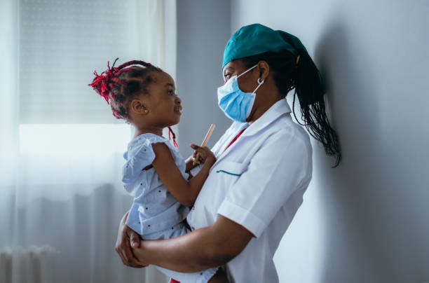 belle femme médecin tenant une petite fille à l’hôpital - patient doctor african descent hospital photos et images de collection