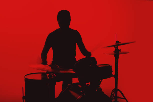 Silhouette of a young man playing drums on a red background.
