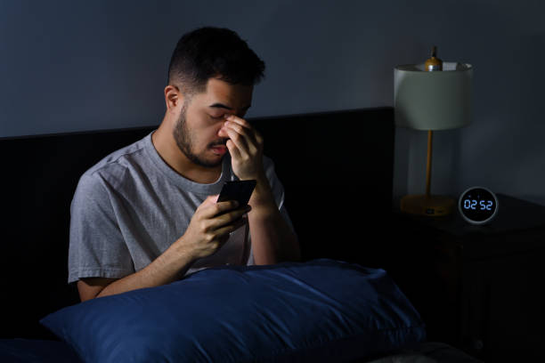 man having sore and tired eyes when using smartphone while lying in bed at night - clock face fotos imagens e fotografias de stock