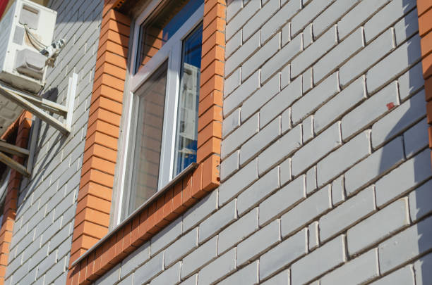 Outdoor air conditioner unit against a white brick wall. A window framed in red brick. Daytime. Selective Focus. No people.