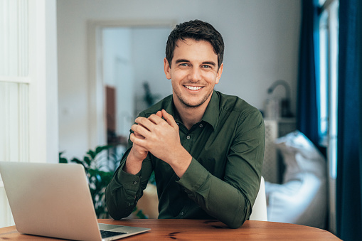 Shot of a young businessman sitting on desk in modern office and looking at camera, smiling