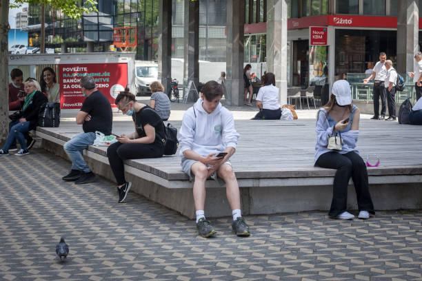 Young people, generation Z, slovenes, boys and girls sitting on a bench watching their smartphones and looking at its content in the streets of Ljubljana. stock photo