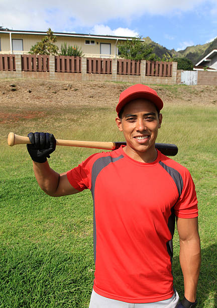 Smiling baseball player poses in a park field Young hispanic baseball player poses in the outfield with his equipment. baseball bat home run baseball wood stock pictures, royalty-free photos & images