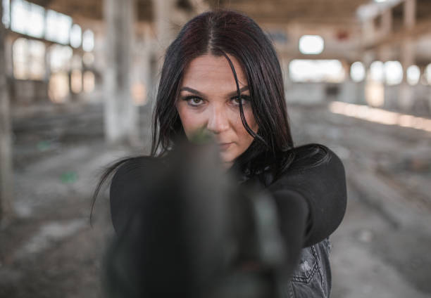 Young woman mercenary assassin with gun in war zone in abandoned warehouse