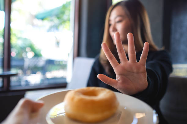 A woman making hand sign to refuse a donut from someone stock photo