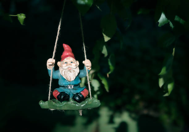 istock Garden dwarf sitting on a swing hanging from a tree, outside in the backyard. 1363021324
