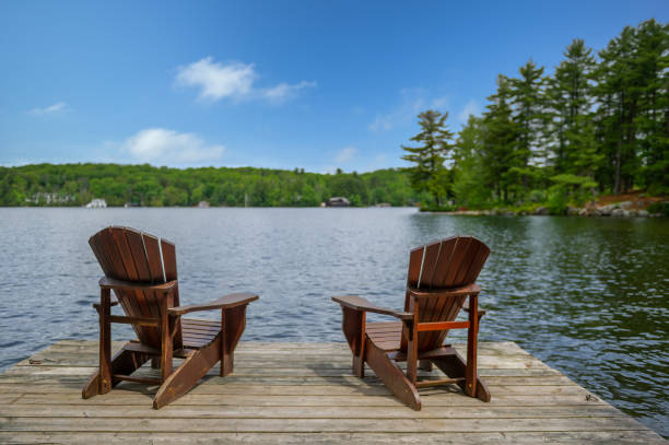 Adirondack chairs on a wooden dock facing a lake in Muskoka stock photo