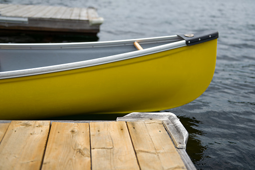 Close up of a yellow canoe tied to a wooden dock on a calm lake in Muskoka, Canada.