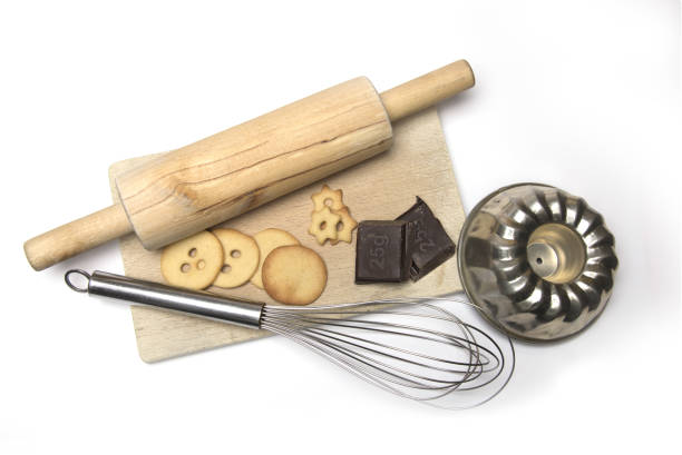 Wooden board with baking utensils cookies and cooking chocolate rolling pin whisk and baking dish on white background