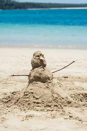 Snowman made from sand on a sandy beach near the ocean. Travel tourism winter tropical vacation