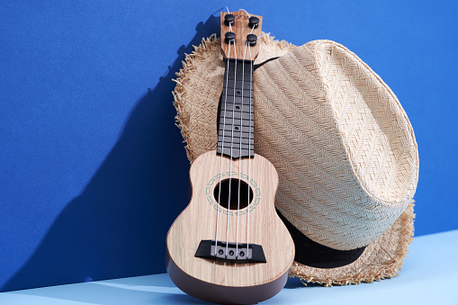 ukelele and straw hat against blue background