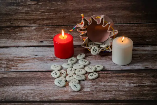 rune stones with black symbols for fortune telling with candles on a wooden table