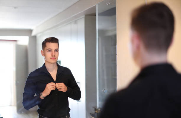 istock A Young man buttoning up his shirt in front of the mirror. 1363047761