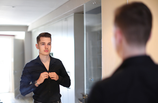 A Young caucasian male buttoning up his shirt in front of the mirror in Cape Town, South Africa.