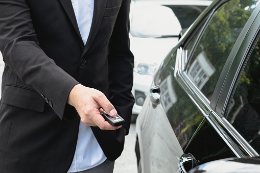 Businessman opens his luxurious car door with a modern remote control key. The young man executive is locking the automobile with the security system. Keyless in male hand.