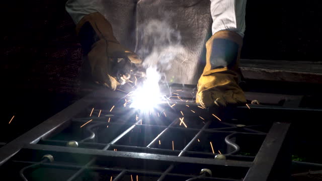 Hand of man wear glove working with arc welding machine to weld steel at outdoor. The welder welds steel reinforcement with welding and bright sparks.