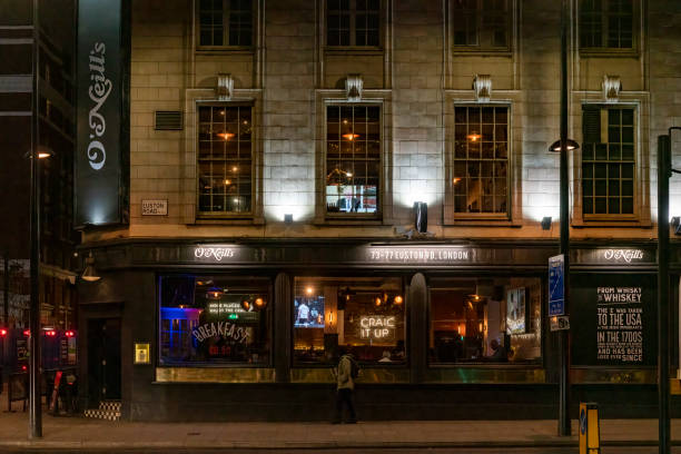 View of city street with restaurant on street corner at night; cars parked along the road; dark blue sky in background