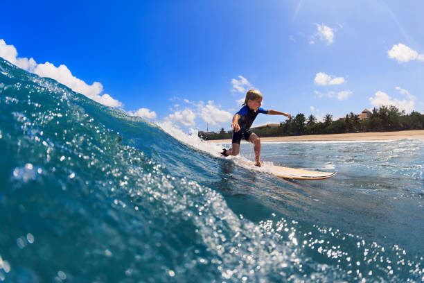 Happy surf boy - young surfer learn to ride on surfboard with fun on sea waves. Active family lifestyle, kids outdoor water sport lessons, swimming activity in surfing camp. Summer vacation with child