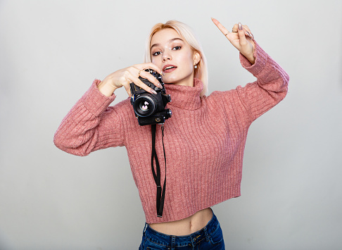 Beautiful blonde woman holding vintage camera on grey background copy space