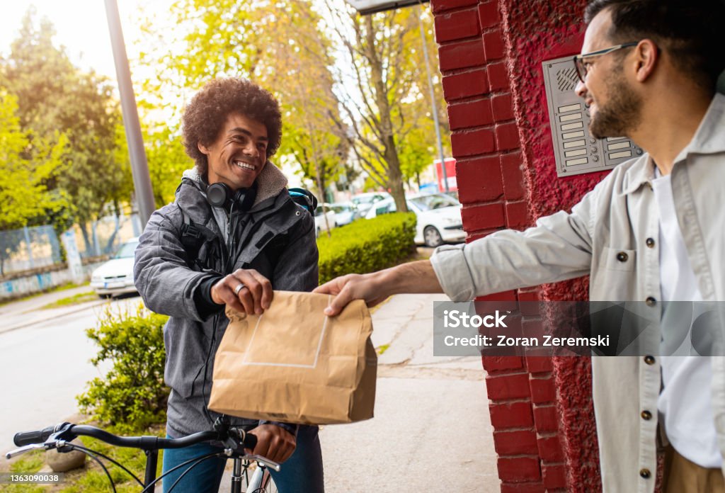 Male courier with bicycle delivering fast food to the customer in city. Food Stock Photo