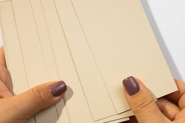 istock Female hands holding stack of gray-brown cardboard rectangular blank tags for clothes with shadows falling on white background. Tag mock up. Copy space 1363090530