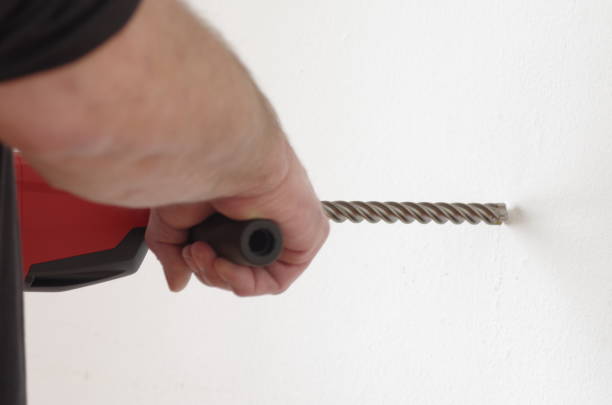 istock Man with drill drills hole in the wall 1363090932