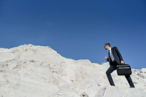 istock Young man businessman with a briefcase and jacket is climbing the mountain. 1363096212