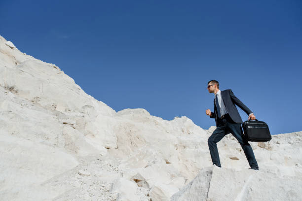 istock Young man businessman with a briefcase and jacket is climbing the mountain. 1363096258
