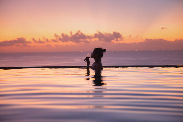 donna asiatica che si gode il vino in una piscina a sfioro al tramonto - infinity pool foto e immagini stock