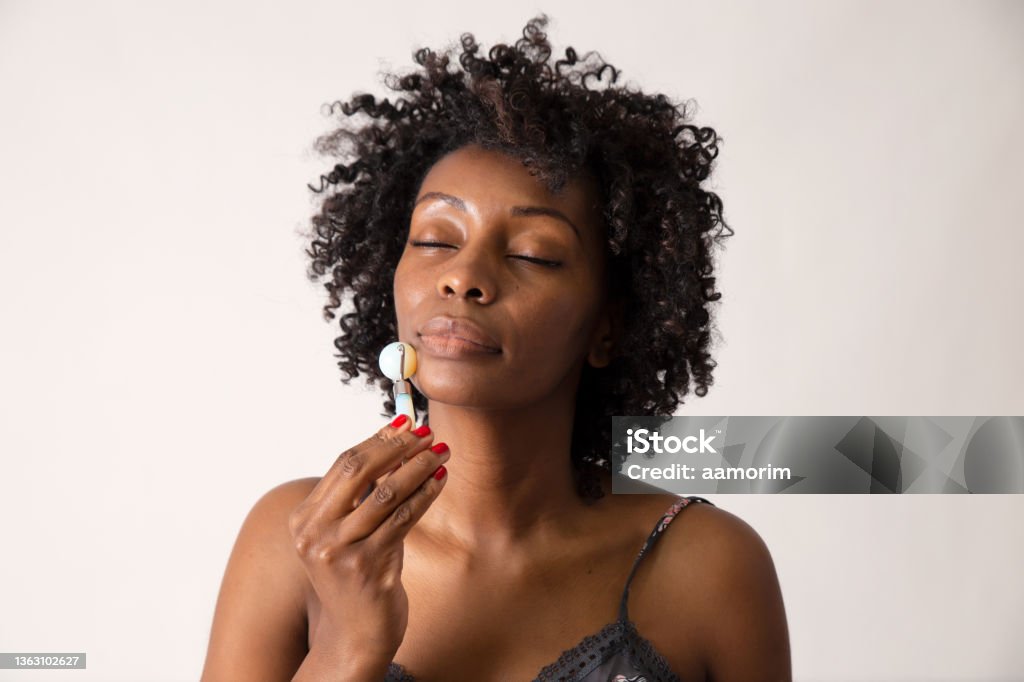 Black woman using a stone face roller Black woman showing how to use a stone face roller Jade Roller Stock Photo