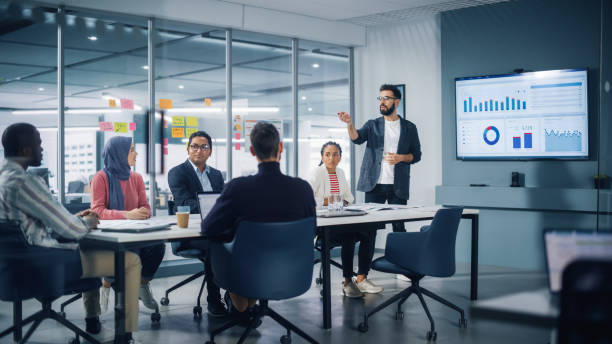 diverse modern office: businessman leads business meeting with managers, talks, uses presentation tv with statistics, infographics. digital entrepreneurs work on e-commerce project. - business stok fotoğraflar ve resimler
