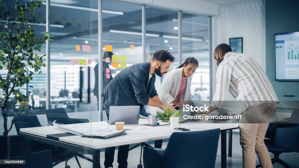 Diverse Team of Professional Businesspeople Meeting in the Office Conference Room. Creative Team Around Table, Black Businesswoman, African-American Digital Entrepreneur and Hispanic CEO Talking. Marketing Stock Photo
