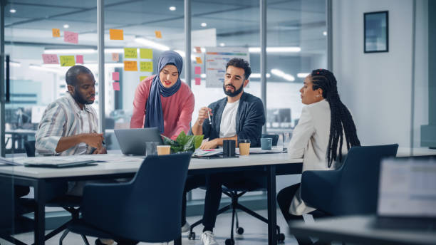 diverse modern office: motivated muslim businesswoman wearing hijab leads meeting, uses laptop, talks of company growth, brainstorms with colleagues. digital entrepreneurs work on e-commerce project - hijab imagens e fotografias de stock