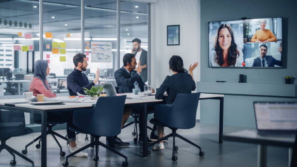 gli uomini d'affari fanno videoconferenza con big wall tv nella sala riunioni dell'ufficio. diversi team di imprenditori creativi a big table hanno discussione. gli specialisti lavorano in digital e-commerce startup - teleconferenza foto e immagini stock