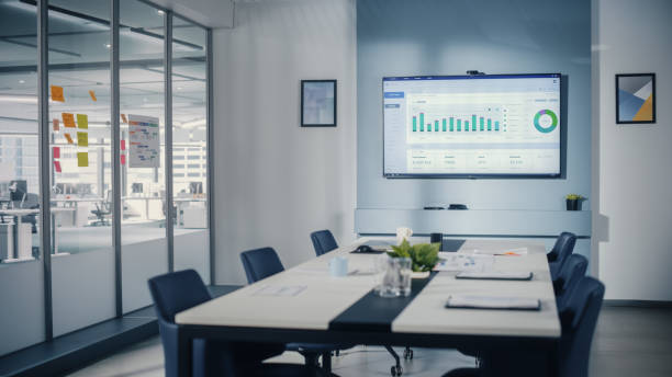 istock Modern Empty Meeting Room with Big Conference Table with Various Documents and Laptops on it, on the Wall Big TV with Big Data Analysis, Charts and Infographics. Contemporary Designed Work Environment 1363105084