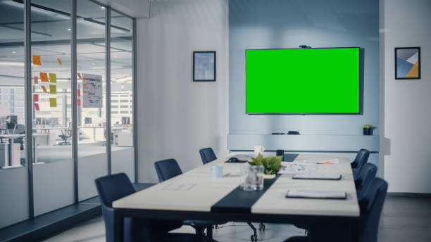 istock Modern Empty Meeting Room with Big Conference Table with Various Documents and Laptops on it, on the Wall Big TV with Green Chroma Key Screen. Contemporary Scandinavian Style Designed Work Environment 1363105162