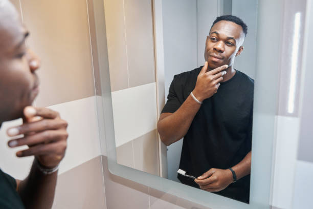 istock Multiethnic male studying his face in mirror of bathroom 1363110302