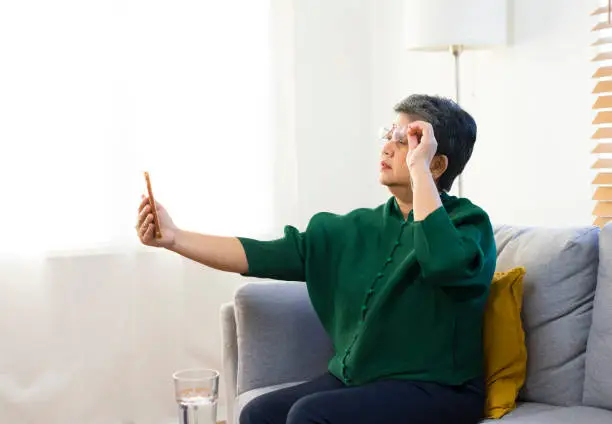 Farsightedness Concept. Elderly woman squinting while looking at smartphone screen, trying to read message.