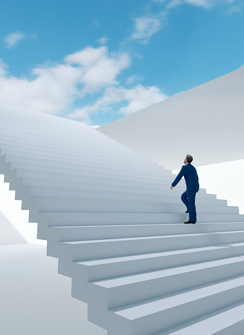 Man in a suit walks a staircase and moves towards the light at the top. Concept image of success and moving your life and career in the right direction.
