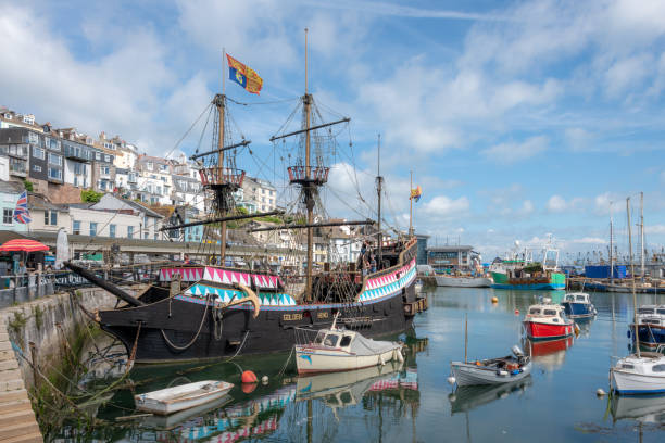 Brixham, UK. 10 August 2021. A replica of the Golden Hind galleon in Brixham Harbour with other boats and the town behind.
