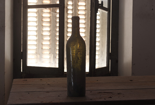 on a wooden table, an old bottle in front of a window with shutters closed in an old house
