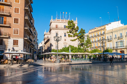 People at a sidewalk cafe near Plaça de la Mare de Déu in Valencia, Spain. In the background is Palacio de la Generalitat Valenciana. This palace, the seat of government in Valencia, was originally designed in 1418.