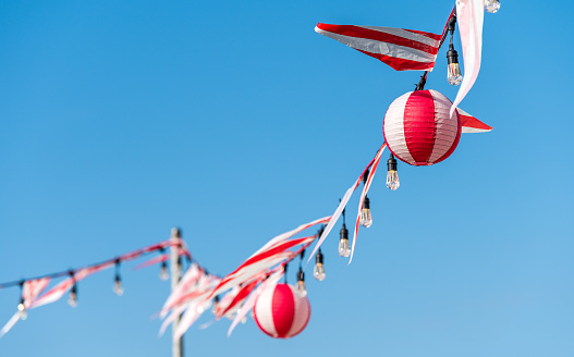 Cheerful clothesline with red and white flags and paper lamps of the same color. Happy image that refers to happy moments of childhood and holidays.