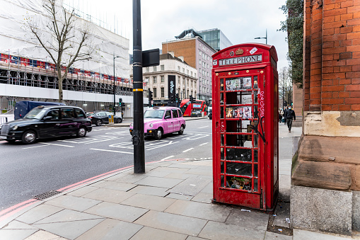 Euston Road outside St Pancras Station and hotel with passengers walking towards the station entrance. London, England, UK. There is a disused red telephone box in the foreground and a black cab behind it.