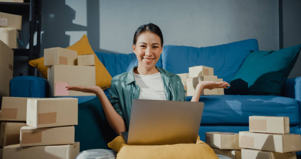istock Young Asian female seller worker online using laptop preparing parcel for shipment to client at home. 1363123312