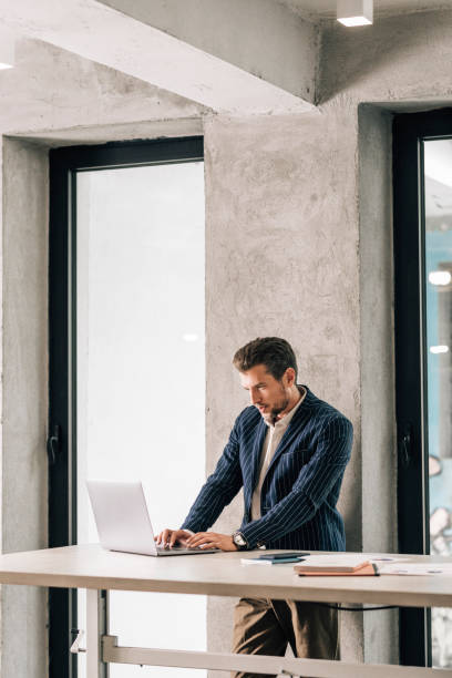 istock Elegant Businessman in a Suit Working at a Standing Desk, Using his Laptop 1363123411