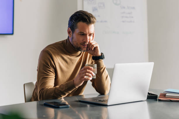 handsome young businessman sitting at the office reading financial reports on his laptop - concentration teacher business copy space imagens e fotografias de stock